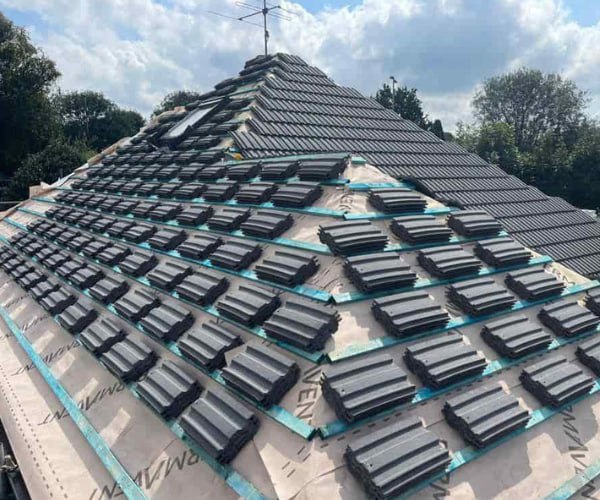 This is a photo of a new hip roof being installed. New felt, battens, and grey tiles have been installed, also a new velux window. Works carried out by BMT Roofing Wollaston