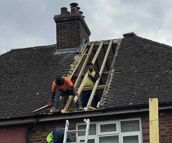 This is a photo of a roof repair being carried out. A section of the roof has been stripped and two roofers are replacing the rafters. Works being carried out by BMT Roofing Wollaston